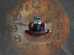 Top-down view of a person in a brown leather chair using a laptop, with a giant clock face in the background.