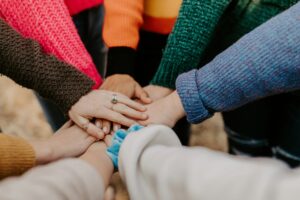 Multiple hands stacked together in the center, wearing colorful sweaters, symbolizing unity and support.