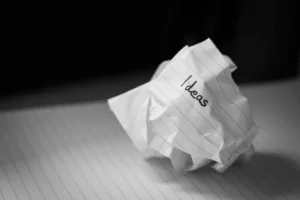 Crumbled notebook paper with the word 'ideas' written on it, resting on lined paper.