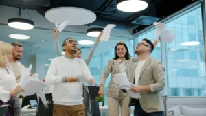 Group of coworkers celebrating in a bright office, tossing papers in the air while smiling.