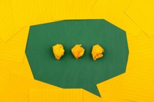 Three crumpled yellow paper balls lined up on a dark green polygonal surface with a yellow, lined background surrounding them.
